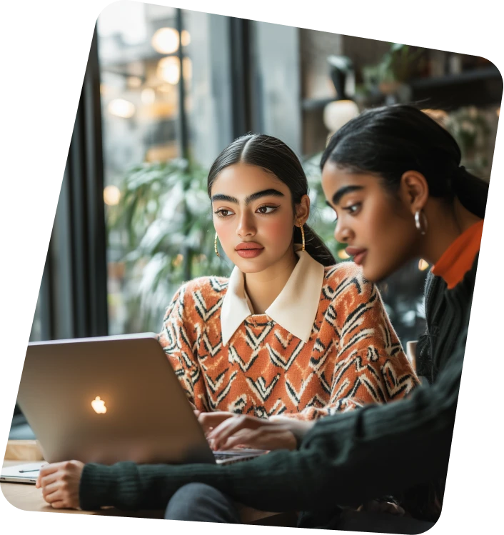 Two women sitting at a table looking at a laptop.