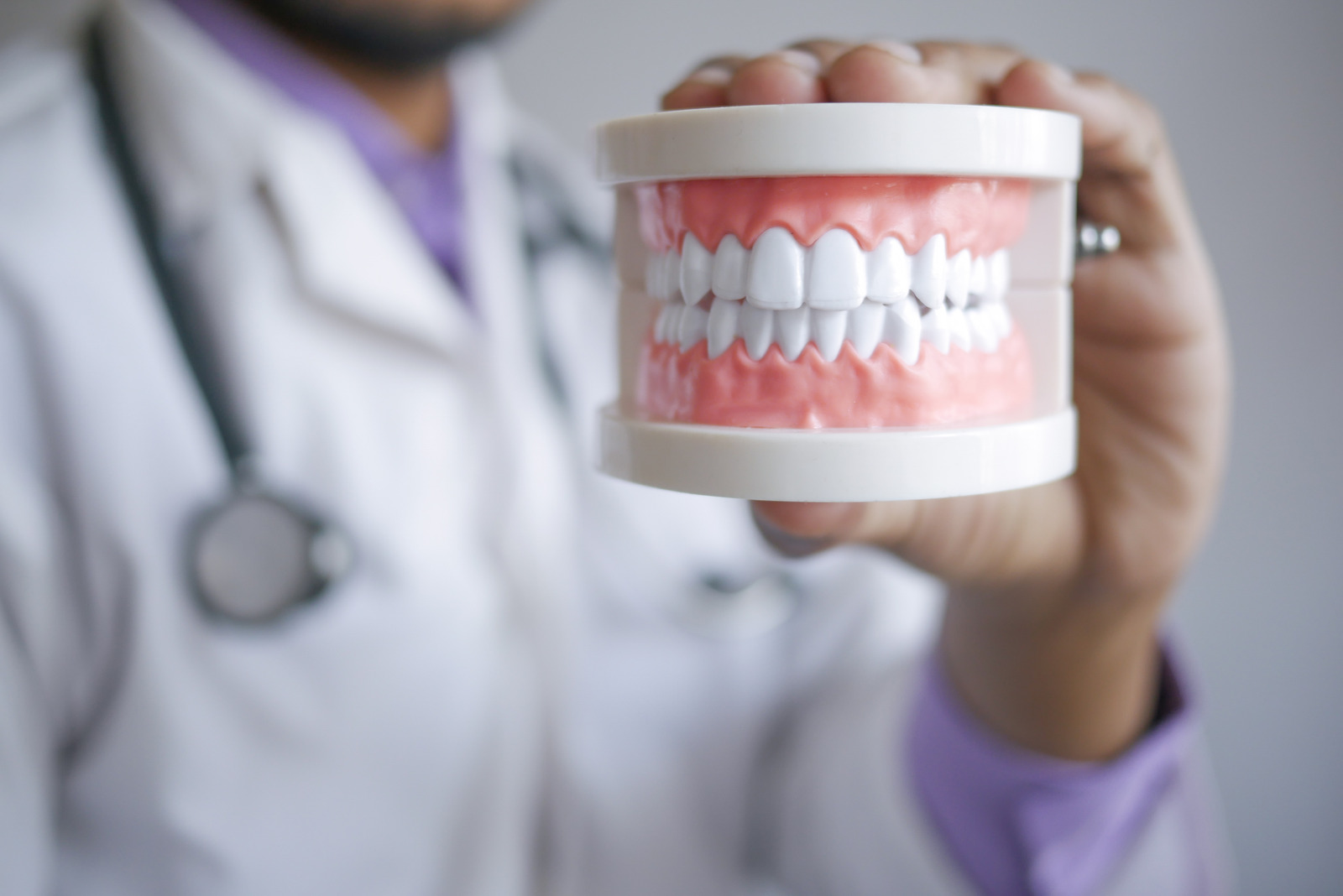 Dentist at Lotus Dental Studio holding a dental teeth model, illustrating dentures vs dental implants