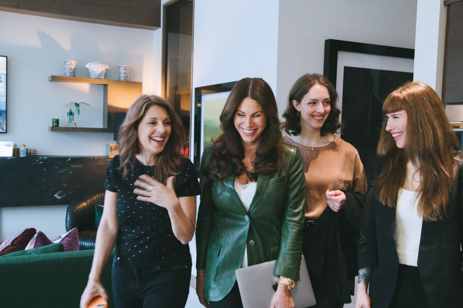 Four women walk together through a modern office, smiling and talking in a relaxed, collaborative setting.