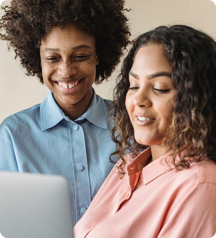Two women smiling and looking at a laptop screen together.