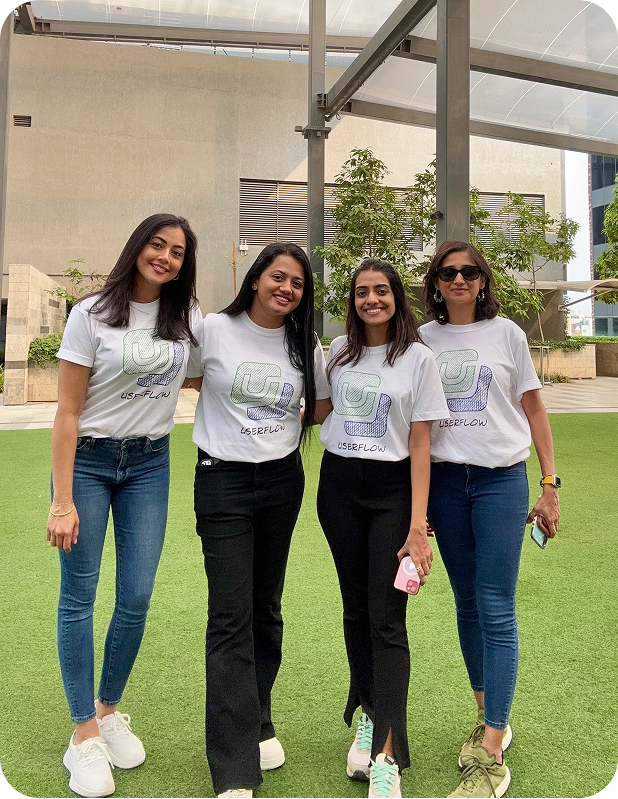 Four women standing outside on green grass, wearing white Userflow logo t-shirts and smiling at the camera.