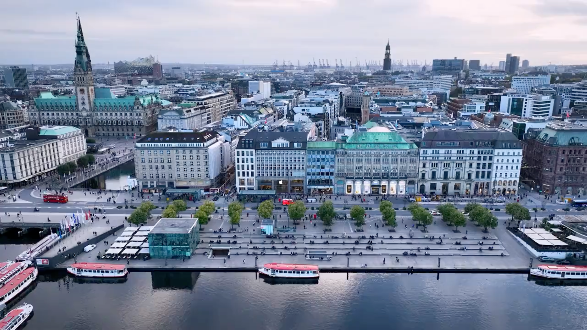Luftaufnahme des Hamburger Rathaus und der Binnenalster mit Uferpromenade, Bäumen und Ausflugsbooten.