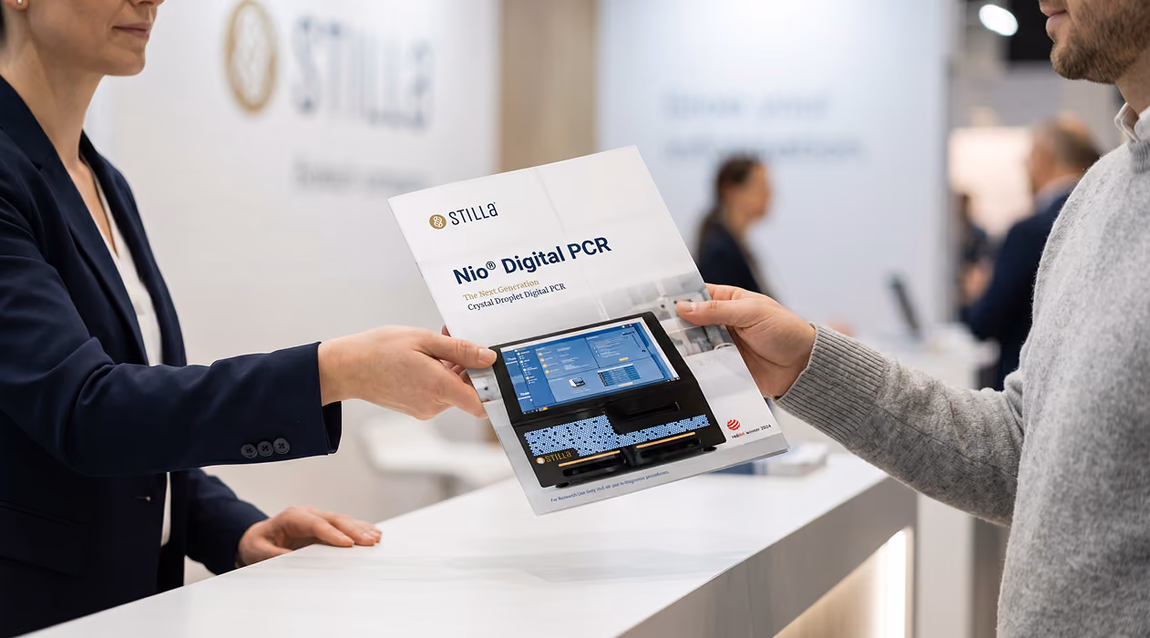 Two people exchanging a brochure titled 'Nio® Digital PCR' with an image of a digital PCR instrument on the cover, in a modern, professional setting.