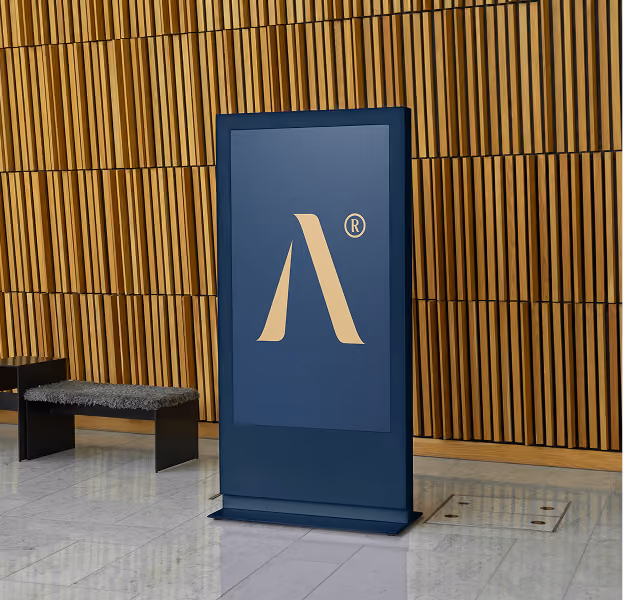 Blue digital display stand with a beige stylized lowercase 'a' and registered trademark symbol in front of a wooden slat wall, next to a bench with a black frame and grey cushion, on a shiny marble floor.