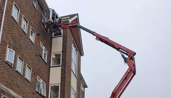 A worker in a cherry picker is repairing the exterior of a tall brick building.