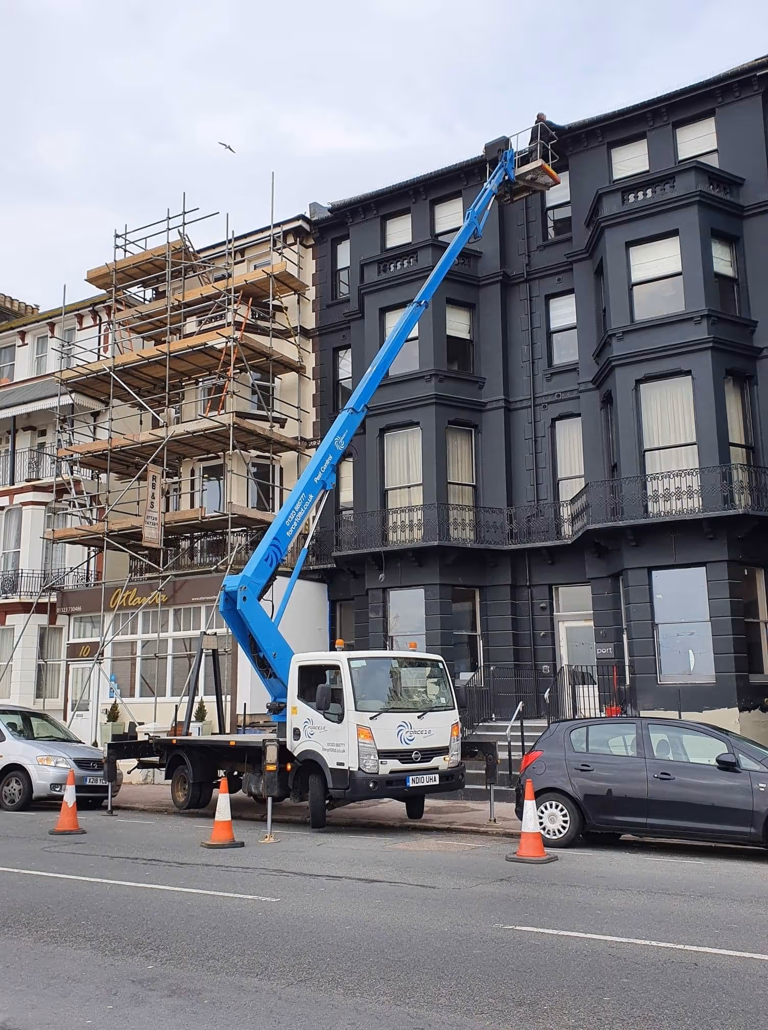A blue crane truck lifts a worker in a basket to the top floor of a building.
