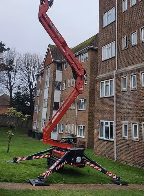 A red cherry picker is positioned near an apartment building, extending its arm upward.