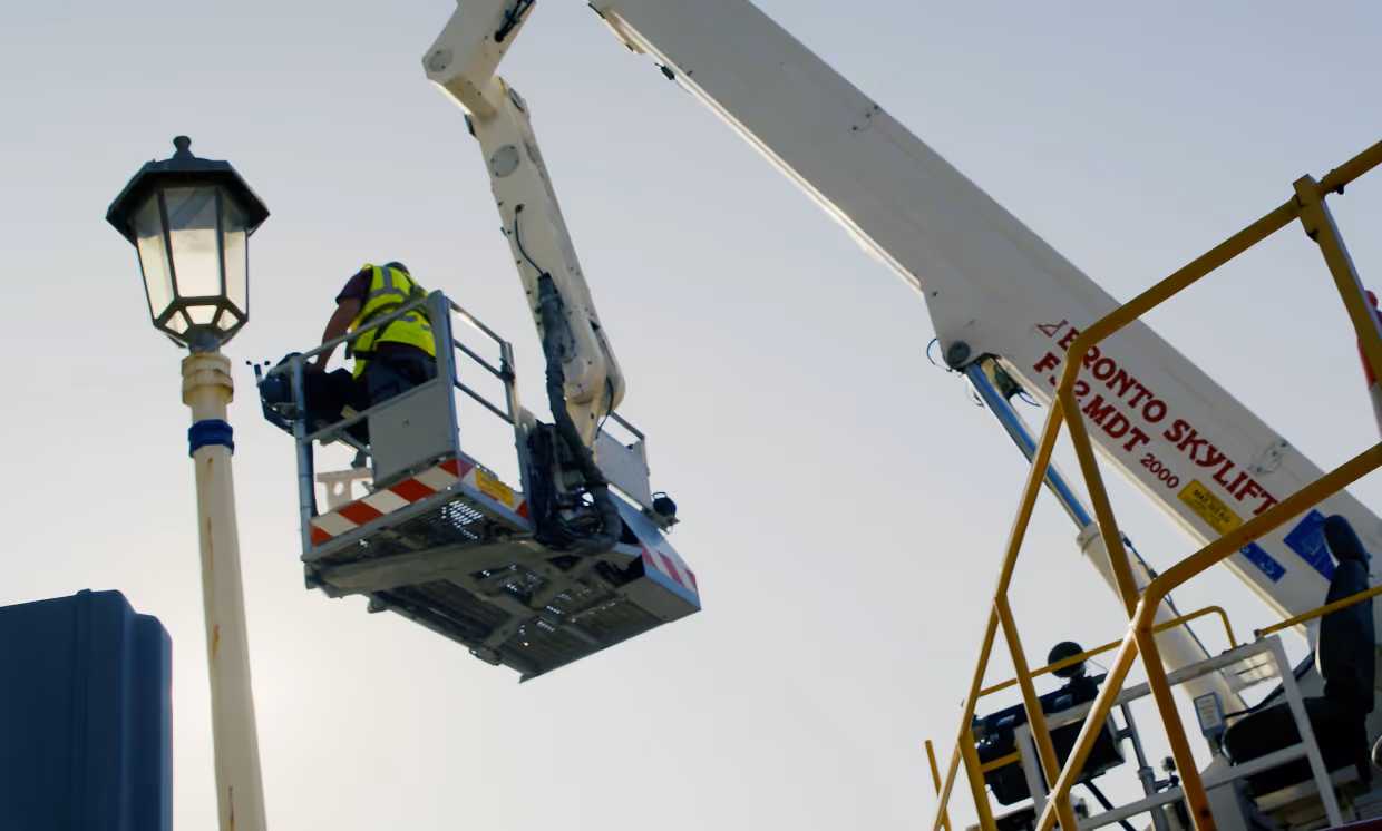A worker in a crane lift repairs a streetlight during the day.
