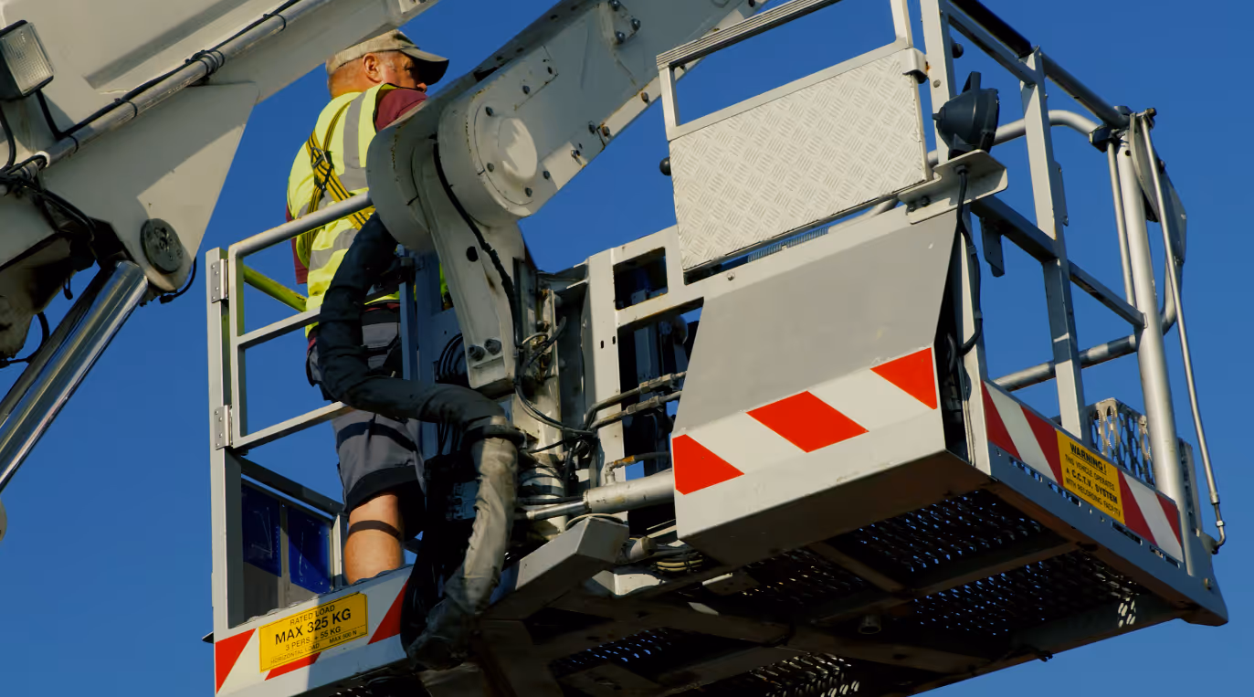 Worker in safety gear operates a hydraulic lift under a clear blue sky.