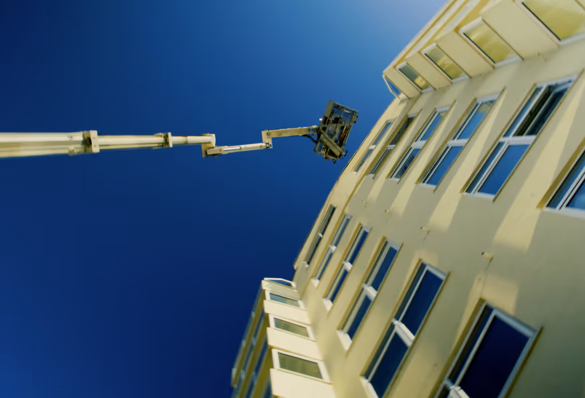 A lift extends towards a tall building for maintenance work under a clear blue sky.