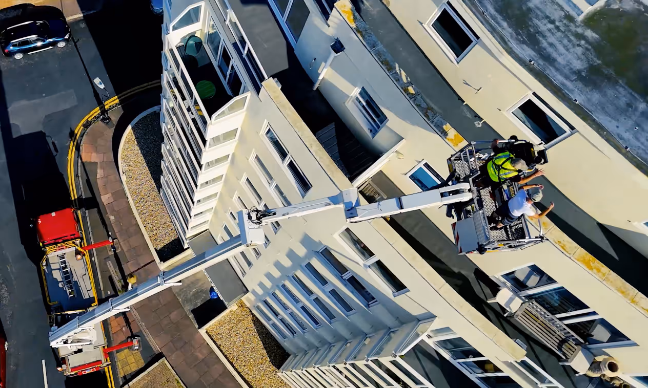 A worker in a safety vest operates a crane lift on the side of a tall building.