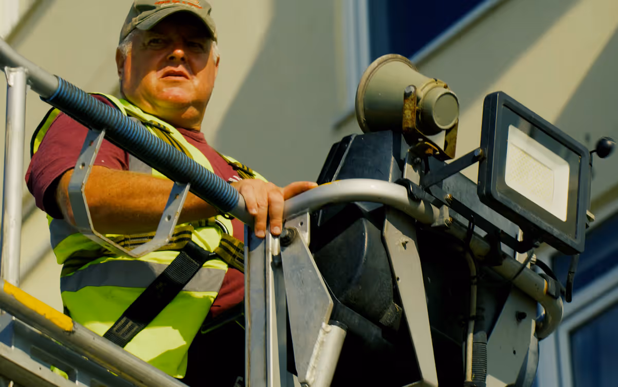 Man in reflective vest operates equipment on an elevated platform outside a building.