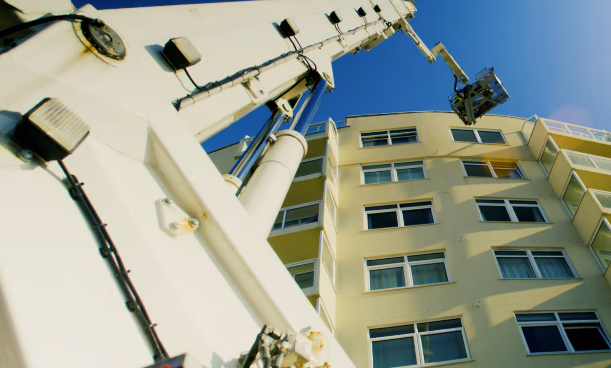A fire truck ladder extends towards the top of a tall building under a clear blue sky.