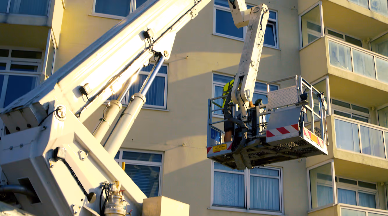 A worker in a lift platform is repairing or inspecting the exterior of a tall building.