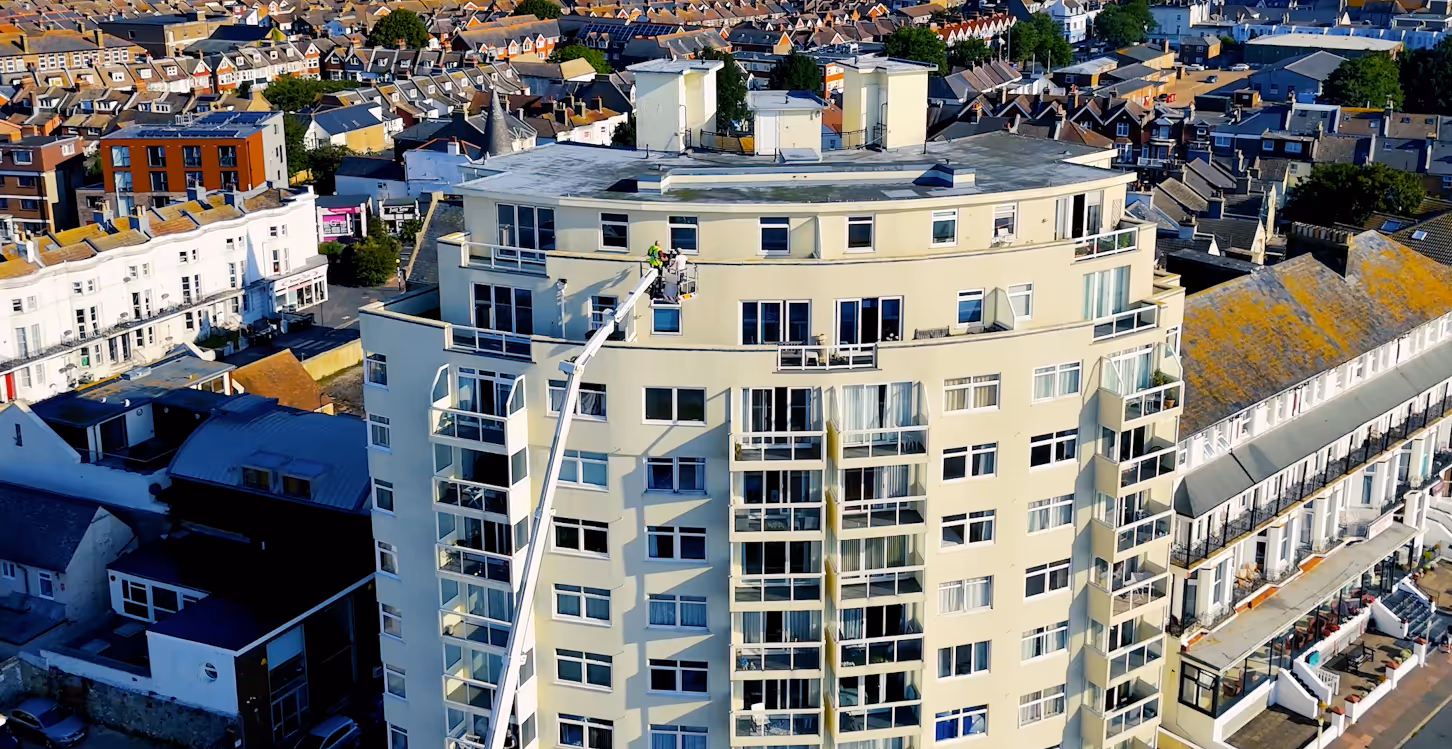 A worker on a lift cleans windows of a tall, circular apartment building.