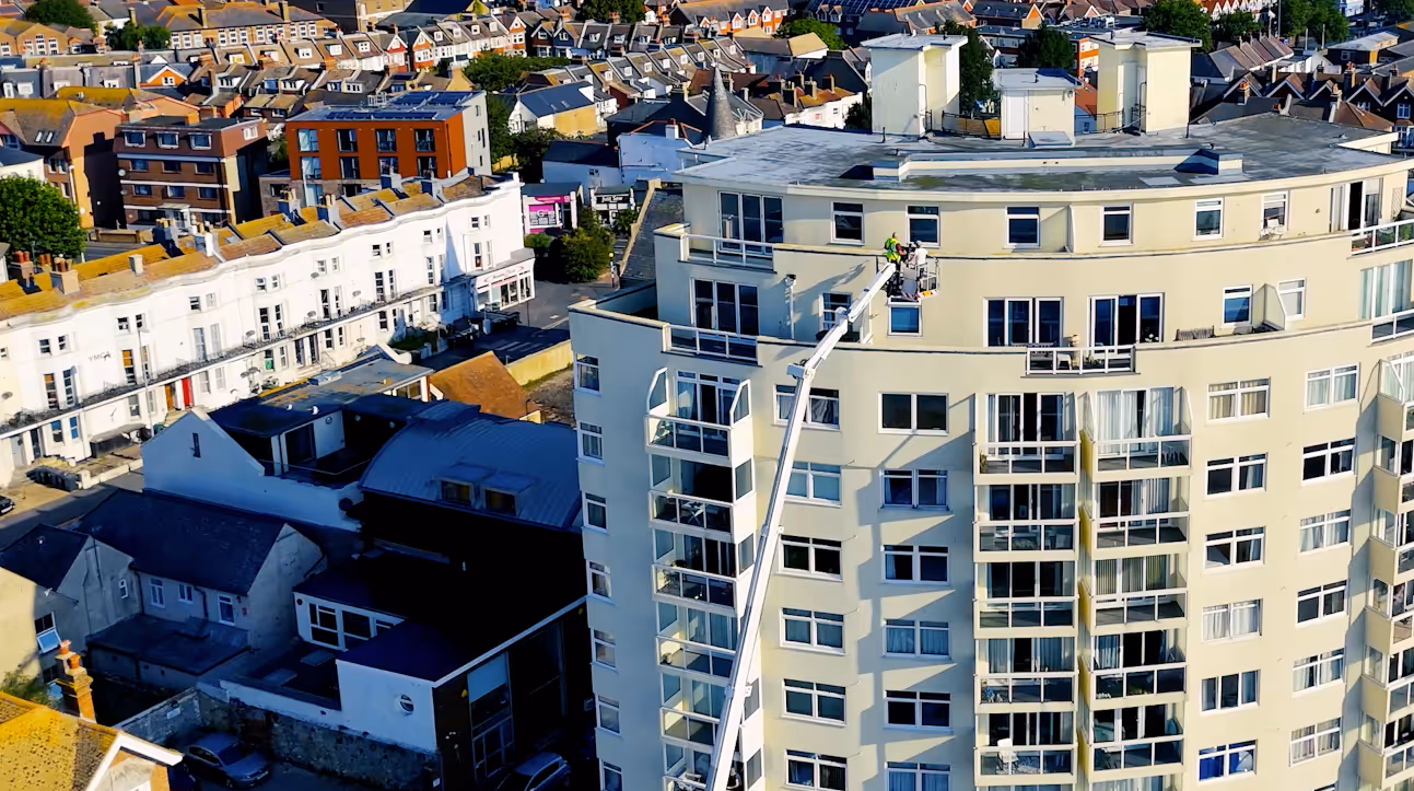Worker washing windows on a high-rise building using a crane lift.
