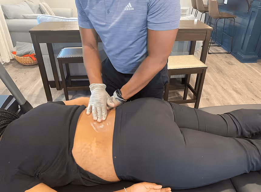 Person in blue Adidas shirt wearing gloves applying ointment on another person's lower back.
