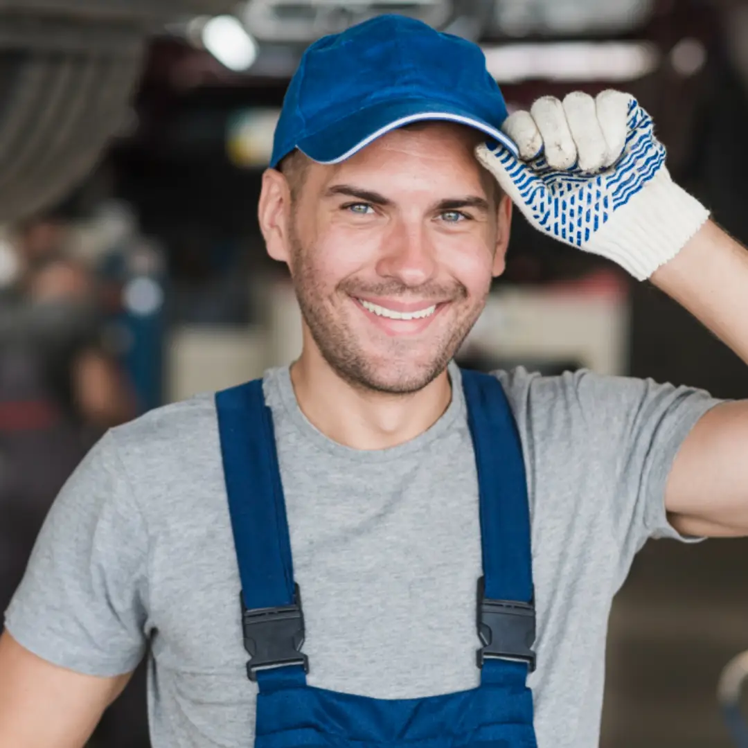 Smiling male worker wearing blue cap, overalls, and work glove lifting his cap.