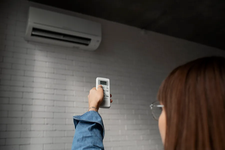 Person holding a remote control and pointing it at a wall-mounted air conditioner.