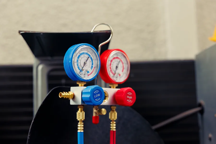 Close-up of blue and red pressure gauges with labeled low and high valves connected by hoses on mechanical equipment.