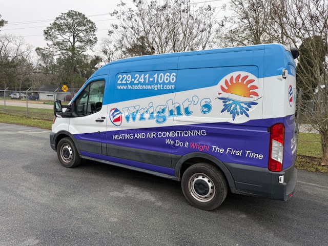 Wright's heating and air conditioning service van with contact number and website, parked on asphalt near trees and a chain-link fence.
