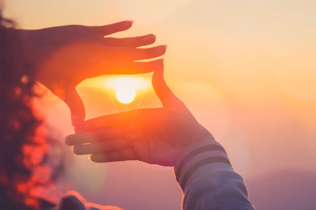 Hände formen einen Rahmen um die untergehende Sonne bei einem orangefarbenen Sonnenuntergang.