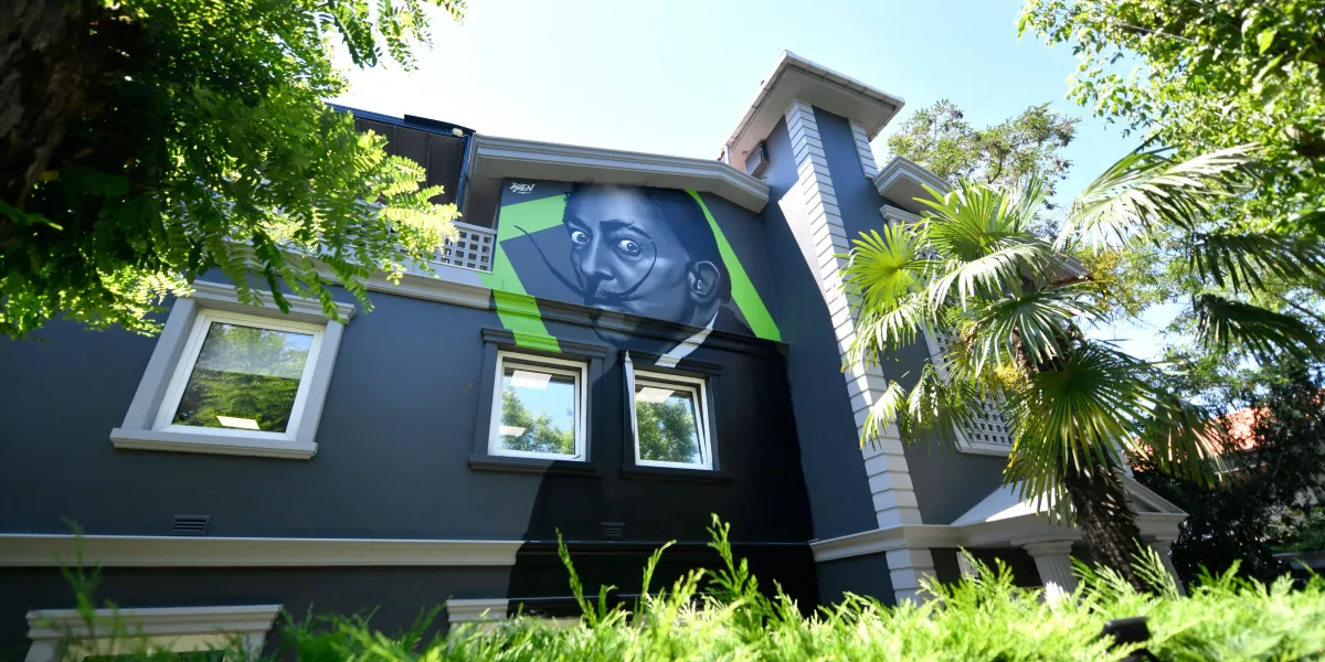 Exterior view of Bizworld's Levent coworking space housed in a charming villa, featuring a striking painting of Salvador Dalí framed by its iconic green branding and logo, nestled amid lush greenery.