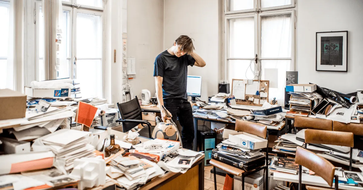 Man standing in a cluttered office, looking stressed amid piles of boxes and papers, illustrating the risks of unmanaged coworking security deposits.