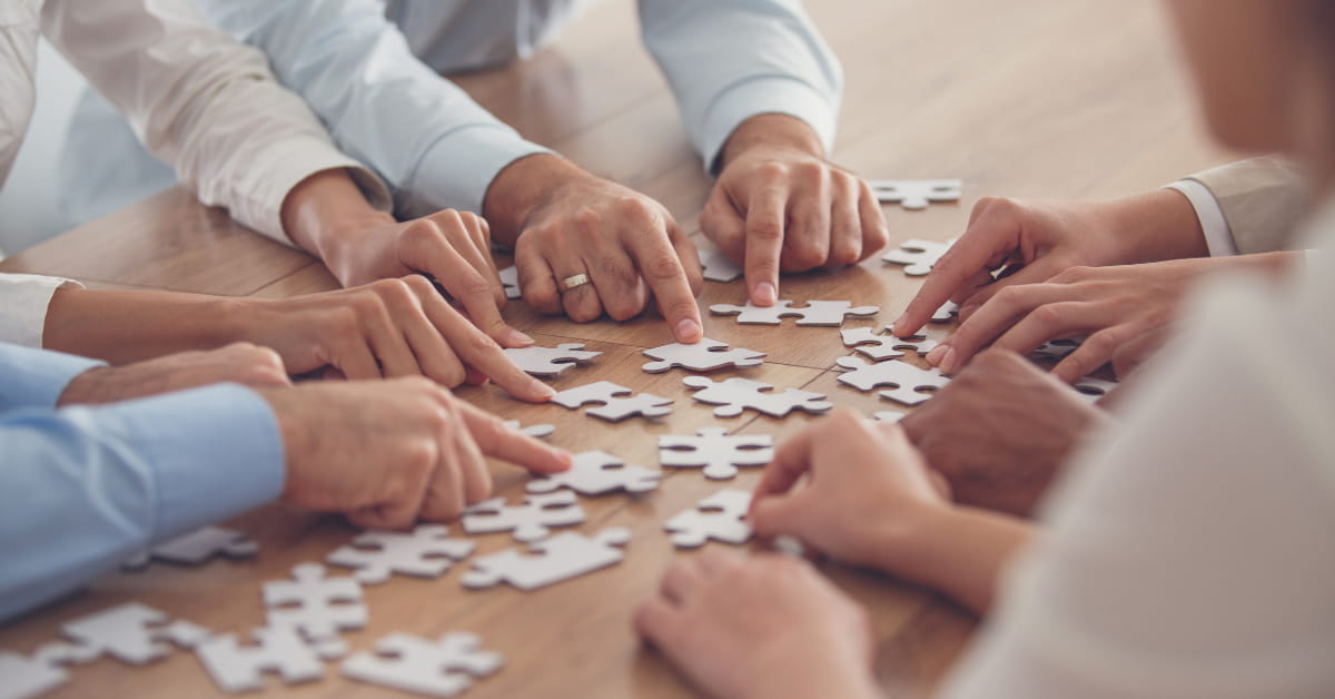 People putting together a puzzle on a desk to signify the coworking industry consolidating. 