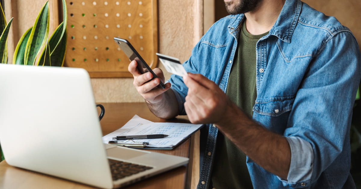 Person holding a credit card and smartphone at a laptop desk, illustrating modern coworking e‑commerce and digital payments.