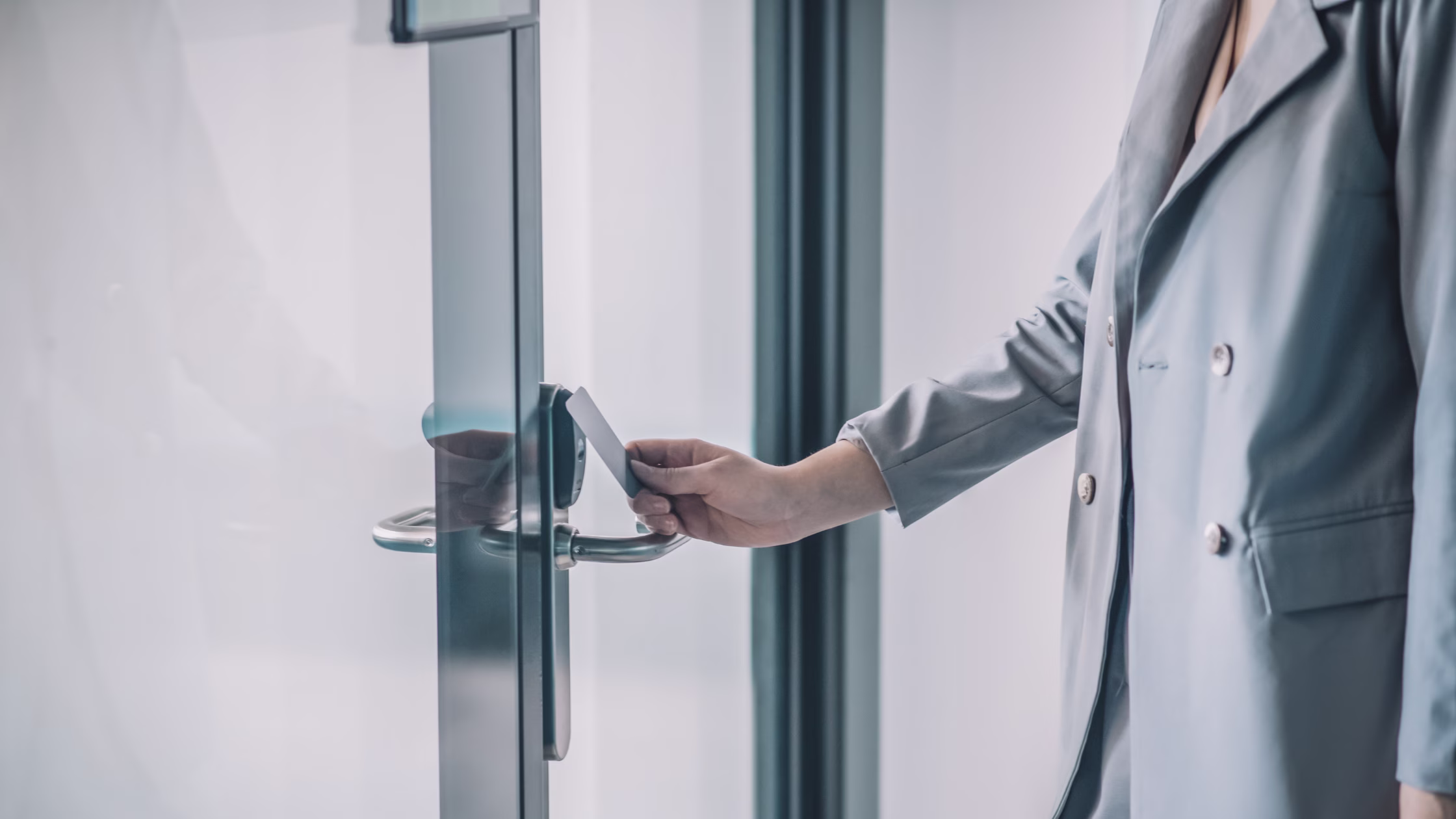 Person using a keycard to access a modern glass office door in a coworking space with an electronic access control system.
