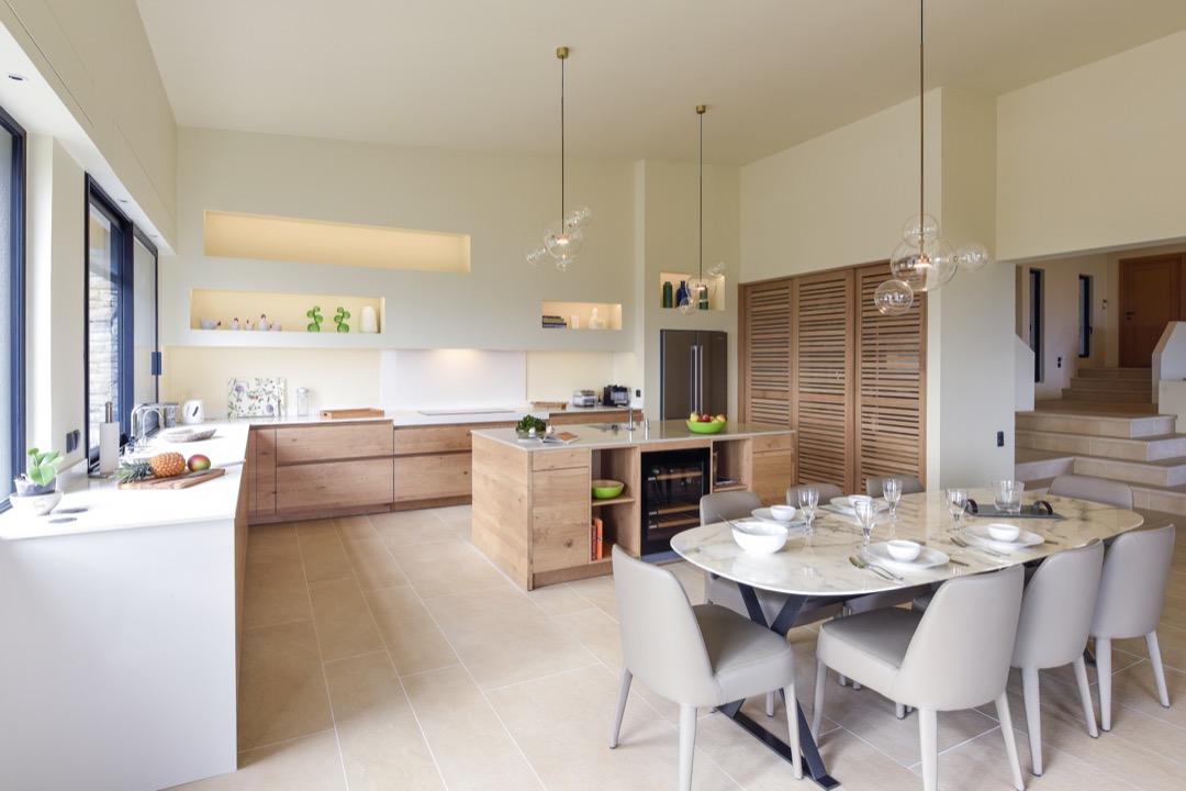 Moderne kjøkken med tredetaljer, kjøkkenøy, spisebord med seks stoler og store vinduer som slipper inn naturlig lys.