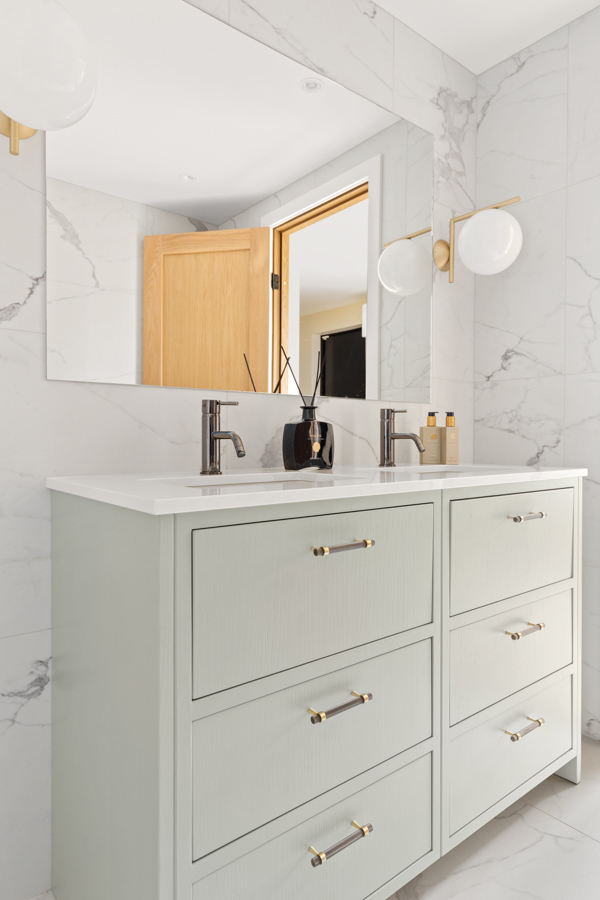 Moderne baderomsinnredning med dobbel servant, store skuffer, marmormønstrede fliser og et åpent tregulv.