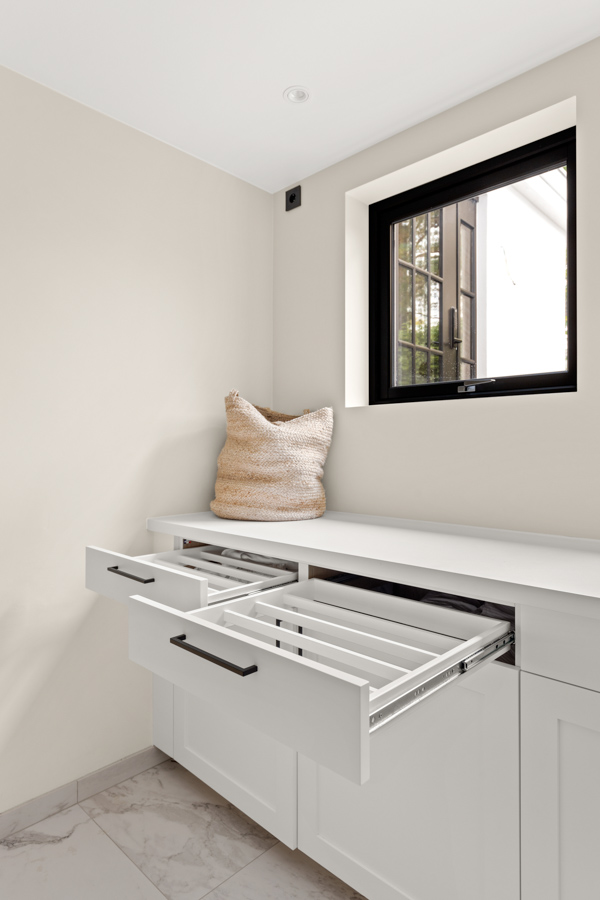 Moderne vaskerom med hvite skap og åpne skuffer under et vindu, med en kurv på benkeplaten.