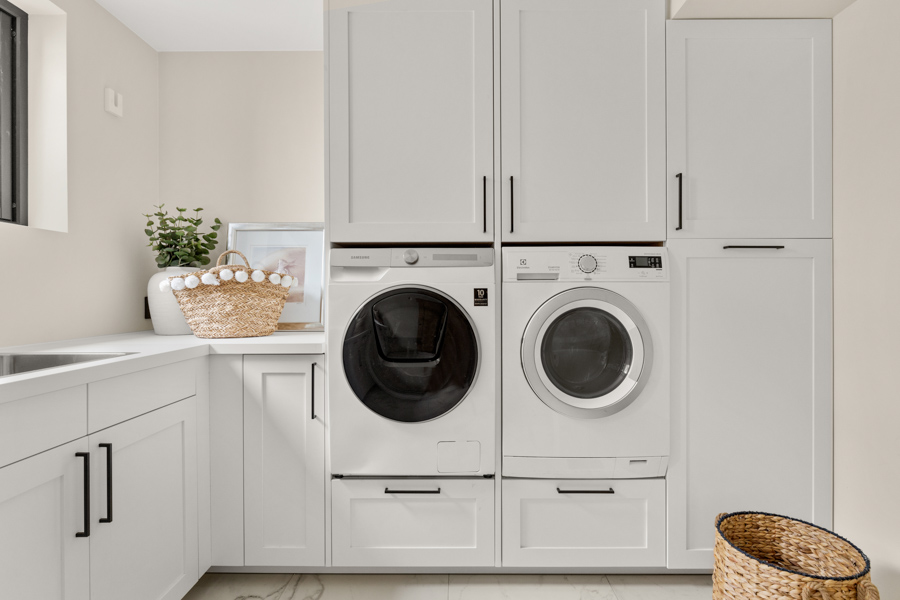 Moderne vaskerom med hvite skap, innebygde hvitevarer, og kurver i flettet materiale.
