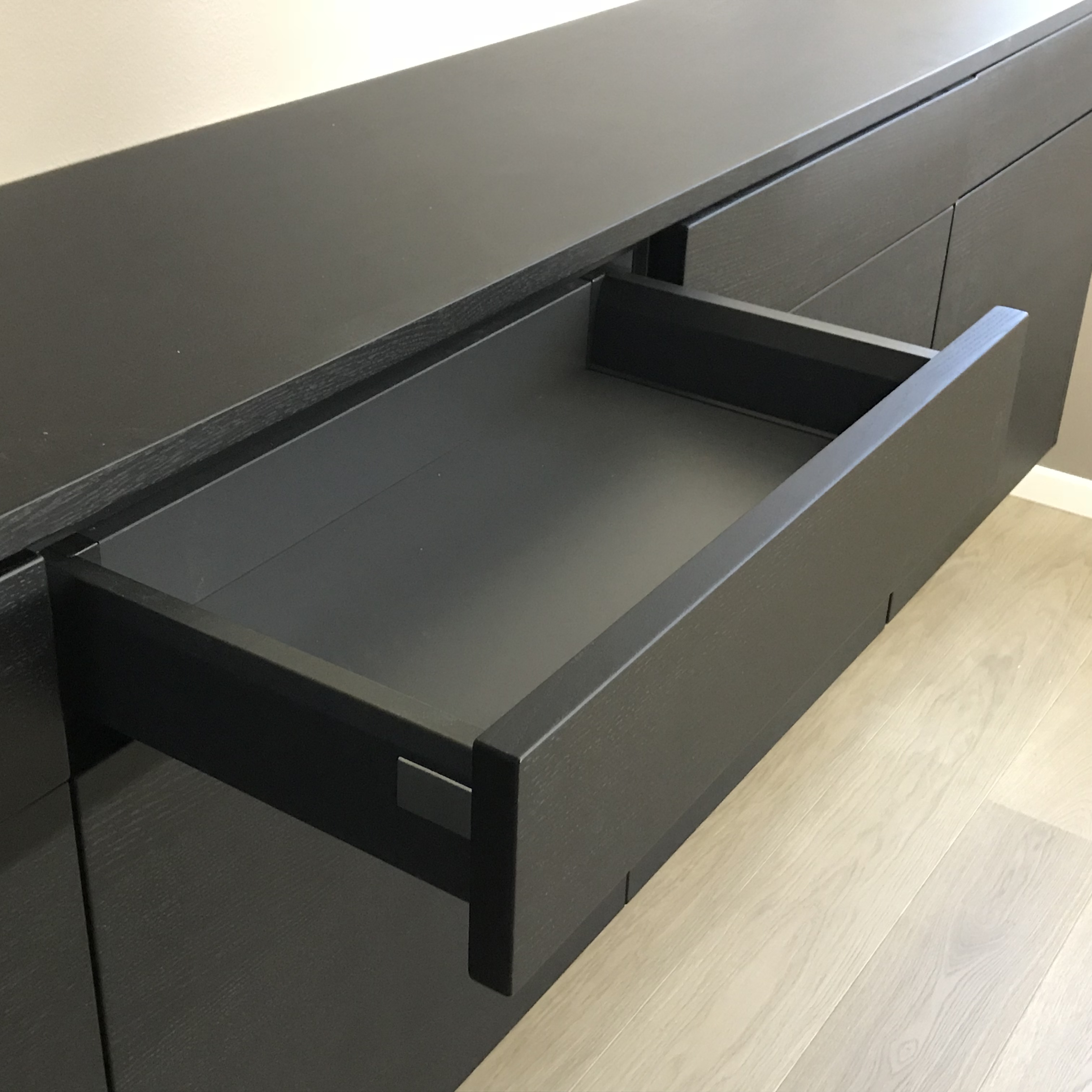 Åpen svart skuff i en minimalistisk kommode på lyst tregulv.