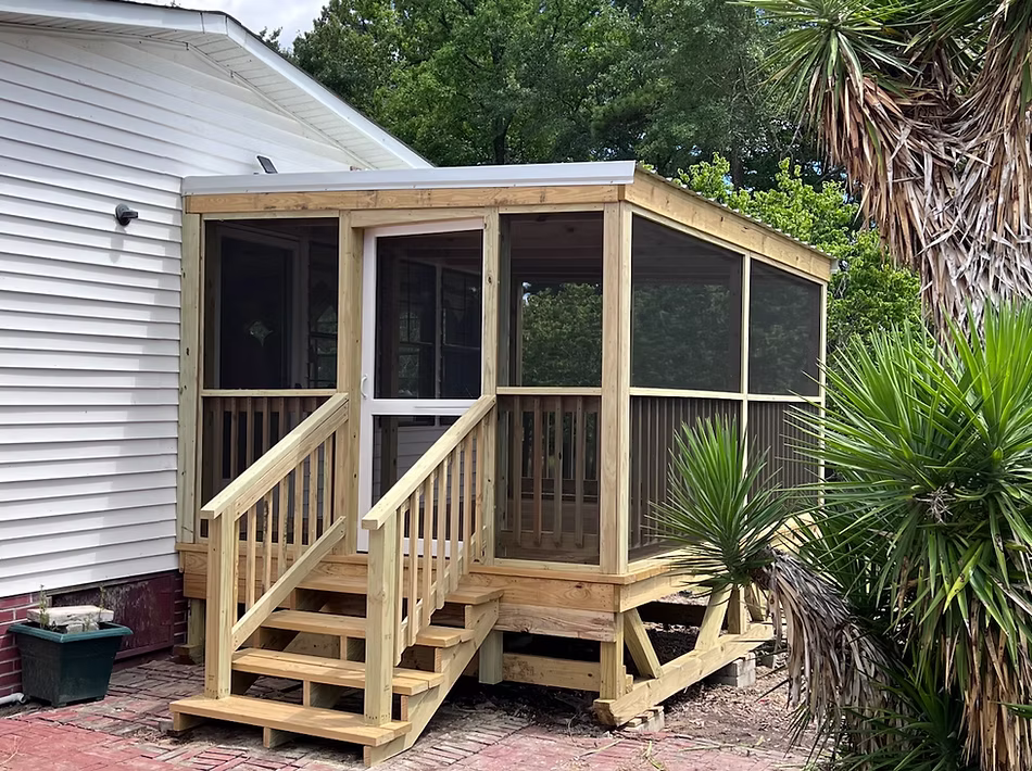 Wooden screened-in porch with doors and stairs attached to house beside palm tree.
