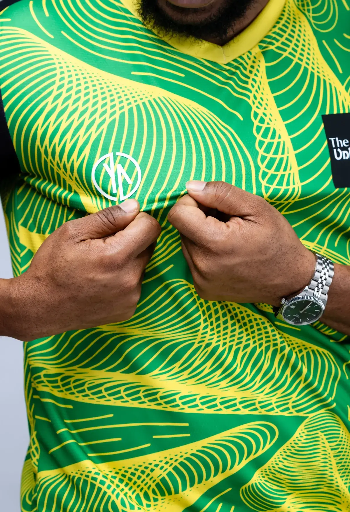Person wearing a green and yellow patterned sports jersey with two fists clenched in front.