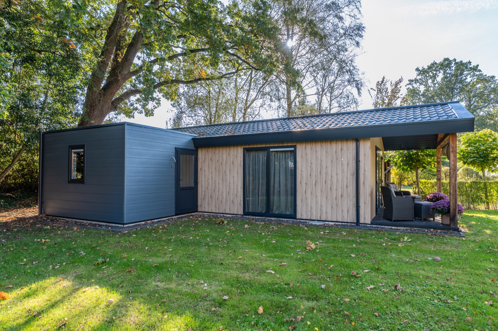 Gelijkvloerse mantelzorgwoning in Enschede met antraciet gevel, houten accenten en overkapt terras in een tuin