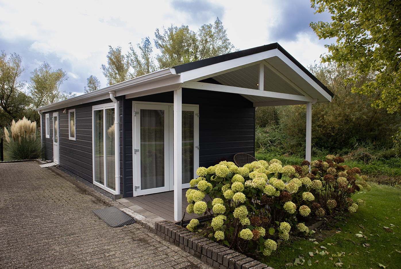 Donkergrijze houten mantelzorgwoning in Dreumel met overkapping en hortensia's
