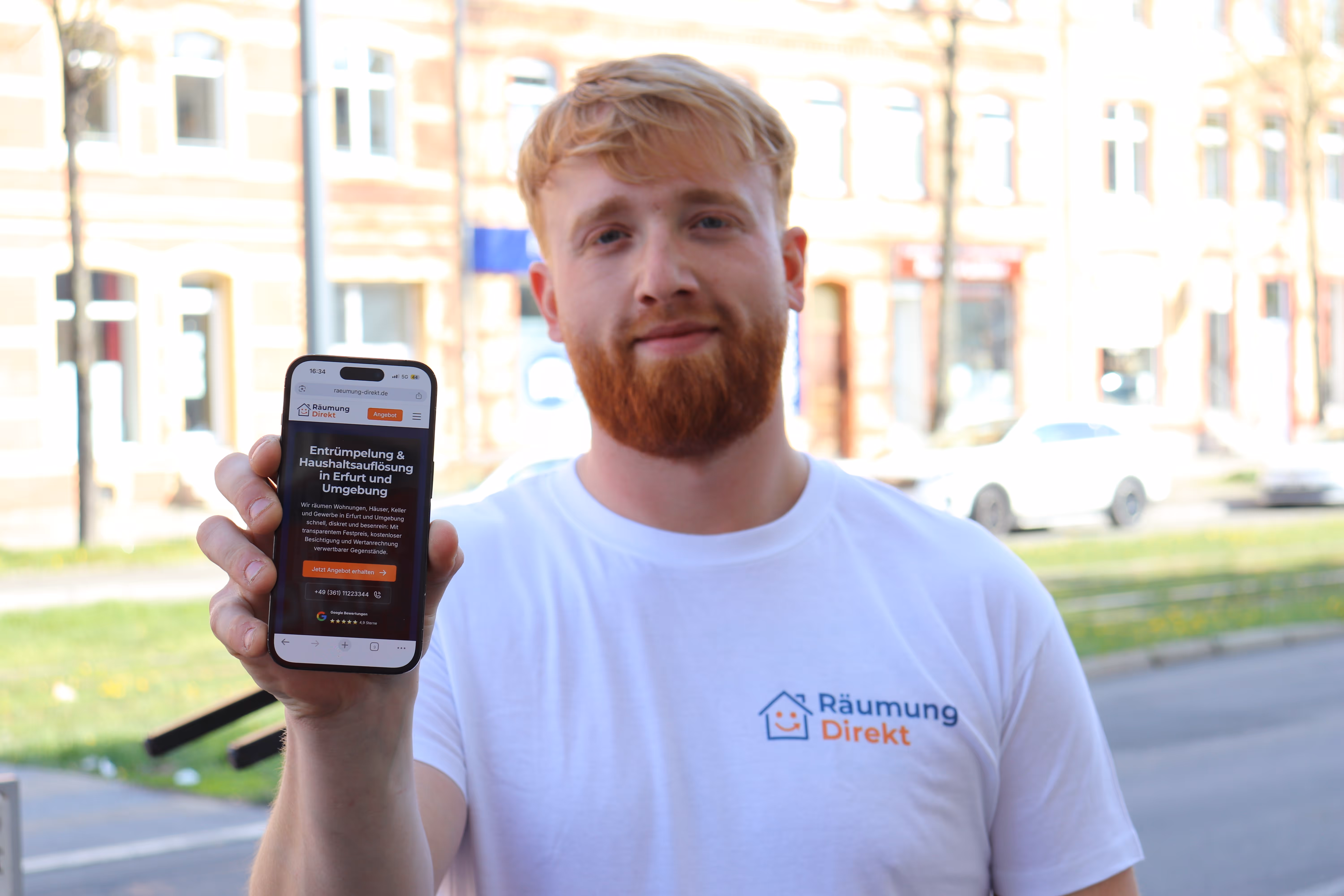 Mitarbeiter in weißem T-Shirt mit Räumung Direkt Logo zeigt ein Smartphone mit einer Website zur Entrümpelung und Haushaltsauflösung in Erfurt.