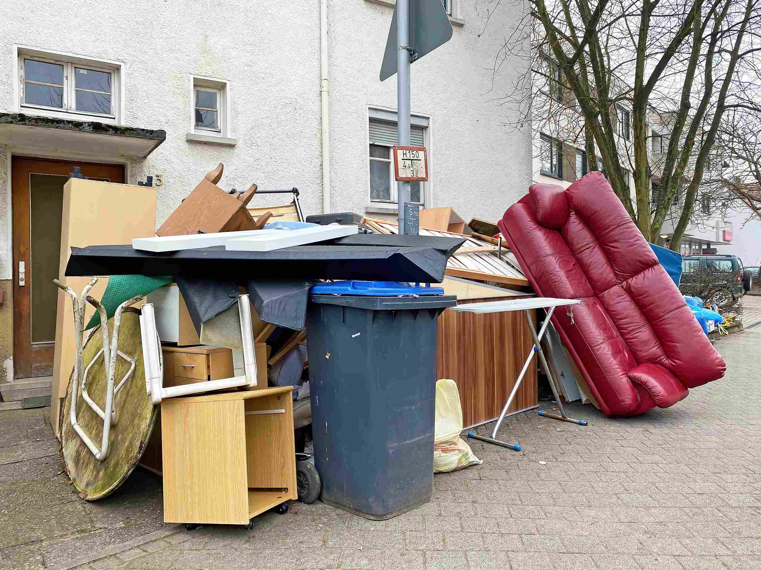 Möbel und Haushaltsgegenstände, darunter ein rotes Ledersofa und ein Wäscheständer, stehen als Sperrmüll vor einem Wohnhaus.