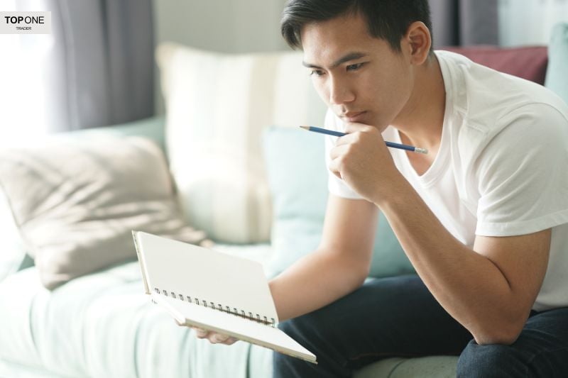 Thoughtful young man holding a notebook and pencil, symbolizing research and planning for choosing the best prop trading affiliate programs