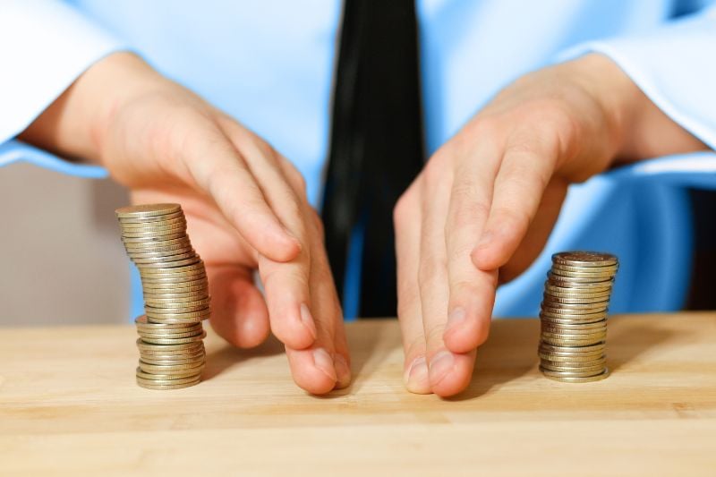 Hands separating two stacks of coins, representing how prop firms make money through profit splits.