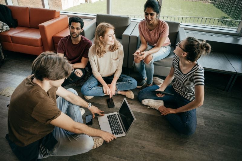 A group of young professionals collaborating on a laptop, discussing strategies and insights into 'how do prop firms make money