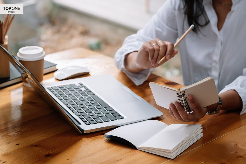 Person taking notes beside a laptop, symbolizing what is a funded trader and the importance of strategy in proprietary trading.