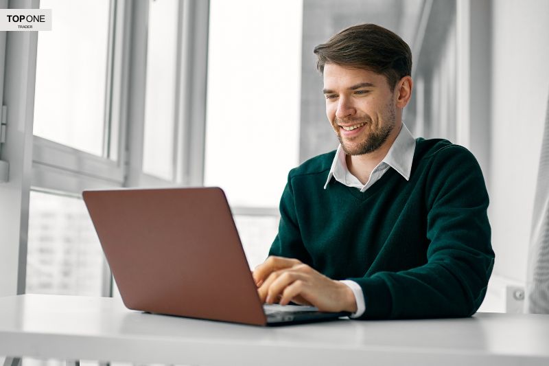 Smiling man trading on a laptop, representing what is a funded trader and the benefits of trading with a firm's capital.