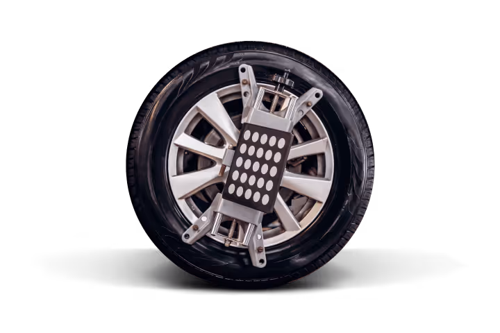 Car wheel with a wheel alignment tool attached to the rim against a black background.
