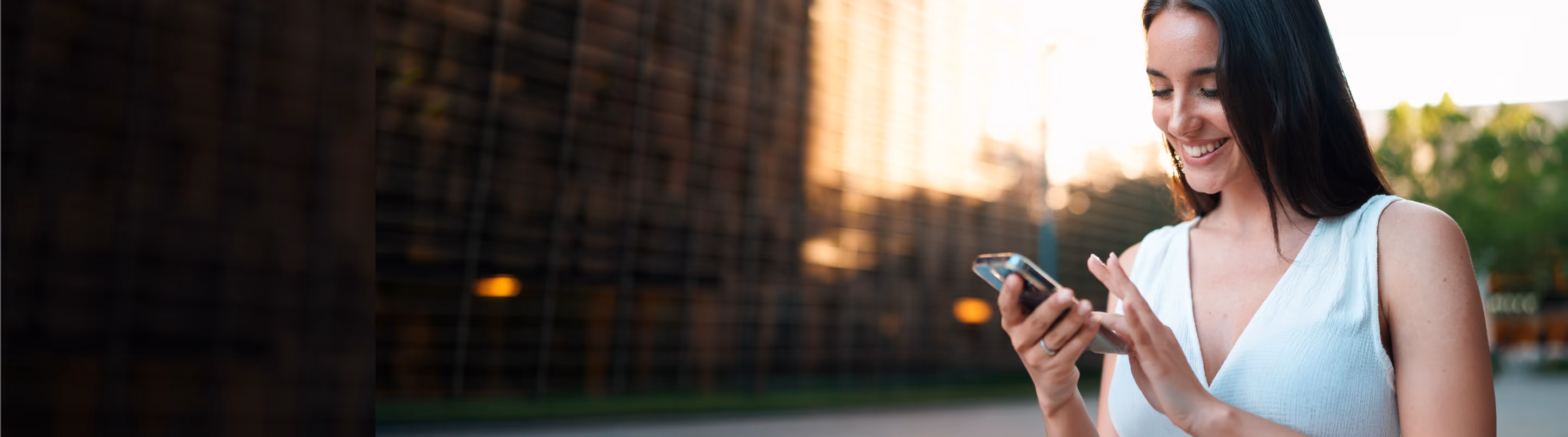 Smiling woman looking at her smartphone outdoors with blurred cityscape background.