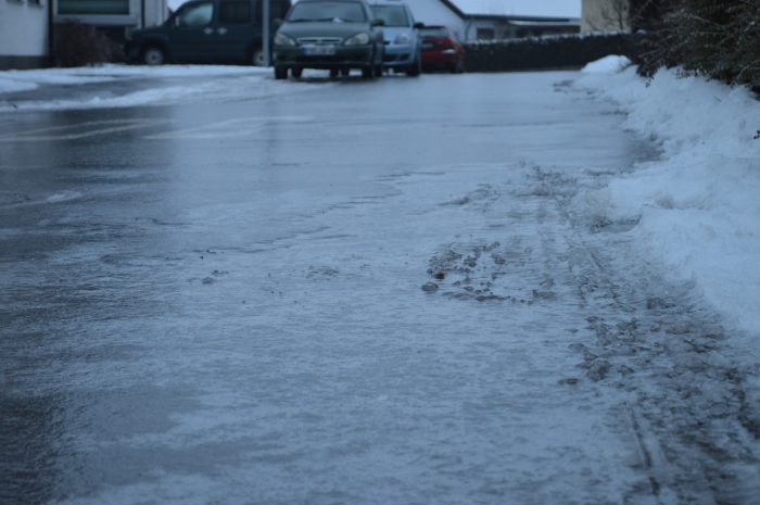 Sheet of black ice in an winter environment. three cars are parked in the distance